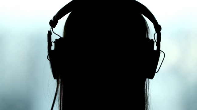 背戴耳机的女人，剪影的人听音乐，歌曲，播客，或有声读物视频下载