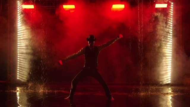 一个男人的剪影与发光的手榴弹在一个黑暗的烟雾演播室。一位时尚的艺人在雨中以红色的烟雾为背景进行火表演。慢动作视频素材
