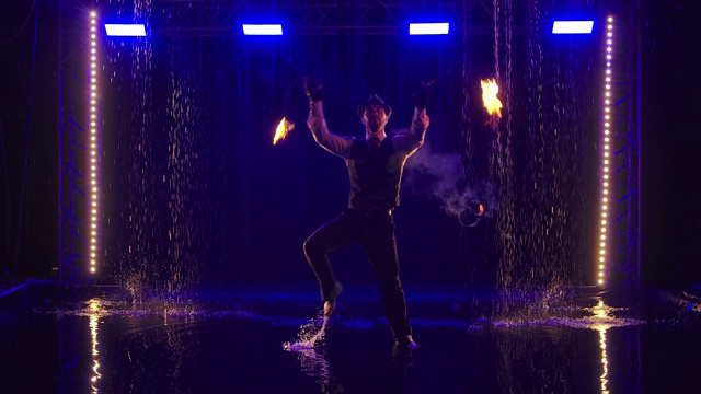 男艺人在晚上用慢镜头表演火表演。在黑暗的演播室里，雨点下的烟火秀。轮廓视频下载