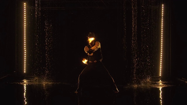 一位时尚人士在雨中表演的令人兴奋的夜火表演。fakir的剪影在一个黑色的背景与演播室舞台灯光。慢动作视频素材