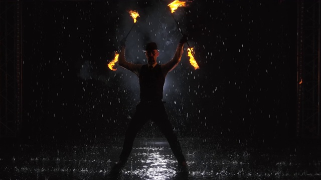 一个人的剪影在一个黑暗的演播室在雨中做一个专业的火表演。慢动作视频素材