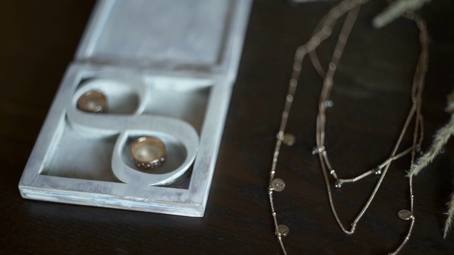 深色木桌上的新娘饰品:新郎和新娘的戒指，木盒里的珠宝，吊坠，金链，花束。慢镜头特写。结婚的那一天。早上准备。锅吧。视频素材