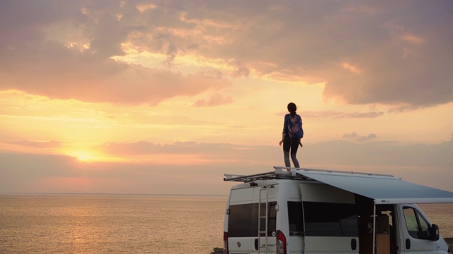 日落时分，一个女人在海边露营车的屋顶上跳舞视频下载