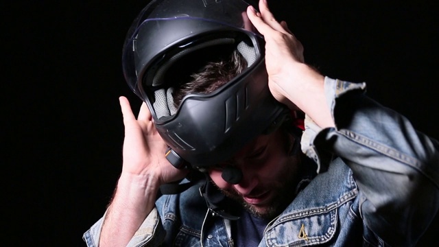 蓝眼睛的中年摩托车手在黑暗的背景下摘掉头盔。视频下载