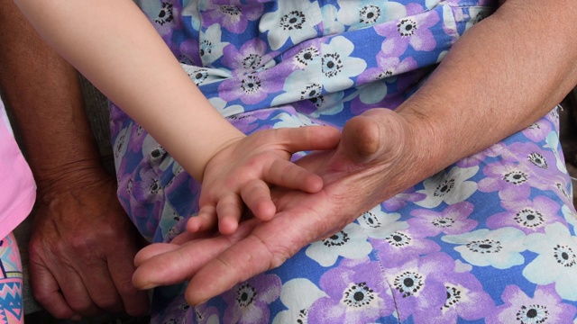 布满皱纹的老手抚摸着孩子柔软的手。孙子和祖母的手的特写视频下载
