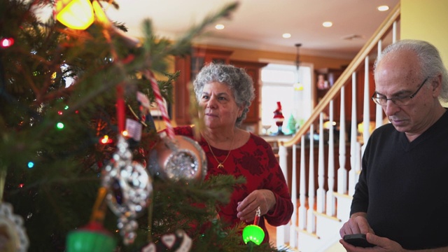 圣诞前夜，这对老年夫妇在美国郊区一个小镇的私人住宅宽敞明亮的客厅里装饰圣诞树。视频素材