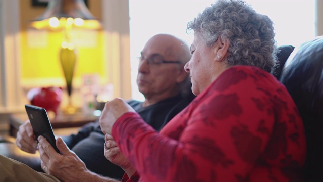 圣诞节期间家庭在线购物。这对老年夫妇坐在圣诞树下的沙发上浏览商品，并使用smartphonу进行购买。视频下载