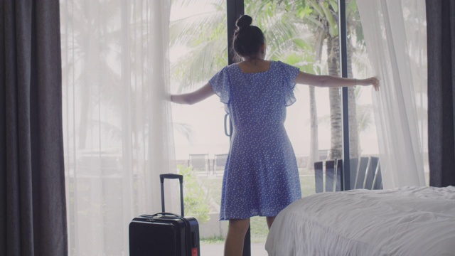 亚洲女性旅行者住在酒店房间里。打开房间的窗帘和门，看看外面的景色。假日旅游概念。4 k慢动作。视频素材