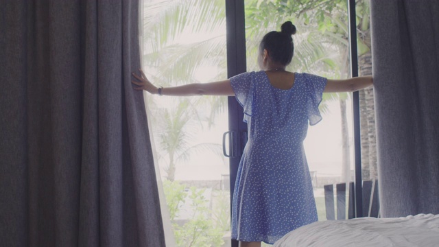 亚洲女性旅行者住在酒店房间里。打开房间的窗帘和门，看看外面的景色。假日旅游概念。4 k慢动作。视频素材