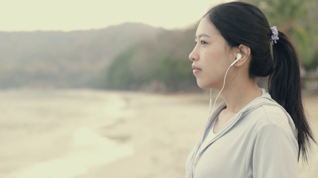 亚洲运动女性穿着运动服，听着音乐，望着大海的景色。视频素材