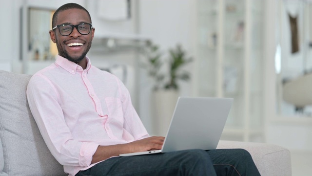 非洲人在家里用笔记本电脑对着相机微笑视频素材