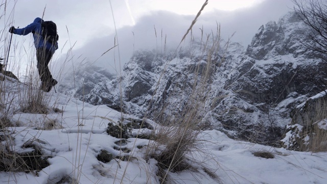 成年男子在冬季徒步旅行，徒步者在雪天爬山。视频素材