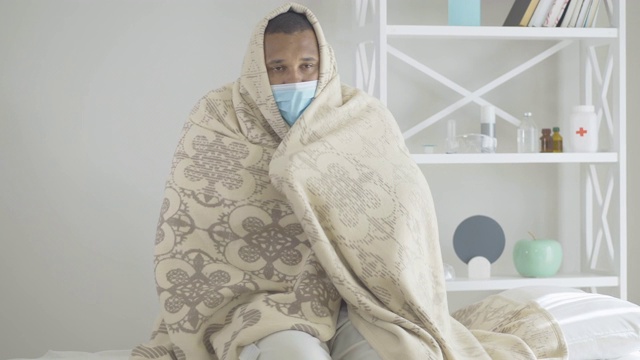 图为坐在医院病床上测量体温的颤抖男子。非裔美国人在室内出现Covid-19症状。一名戴口罩、裹着毯子的男子感染了冠状病毒。视频素材