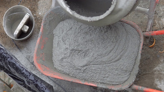 混凝土搅拌机将湿水泥倒入手推车中。电动混凝土搅拌机将湿水泥倒入手推车的特写画面视频下载
