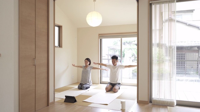 日本一对中年夫妇在日式房间里用平板电脑做伸展运动。视频购买