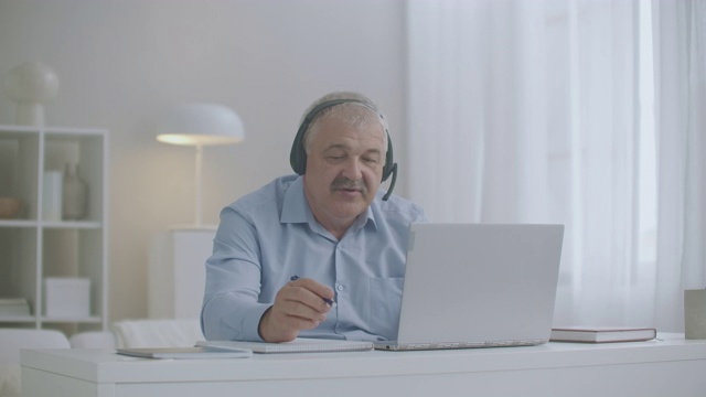 一名中年男子在家使用笔记本电脑和耳机与同事和员工在线聊天视频素材