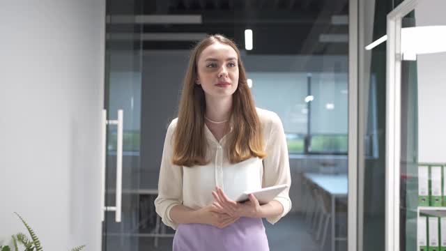 一位年轻美丽而自信的女商人手里拿着一个平板走过办公室的走廊视频下载