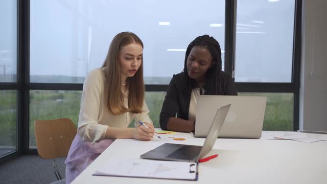 两个年轻的现代多民族商务女性用一台笔记本电脑一起工作视频下载