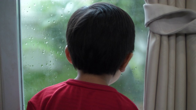 亚洲男婴望着窗外看雨，在家学习想象视频素材