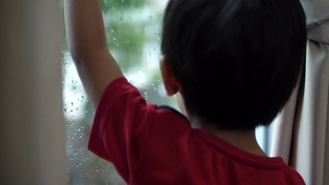 亚洲男婴望着窗外看雨，在家学习想象视频素材