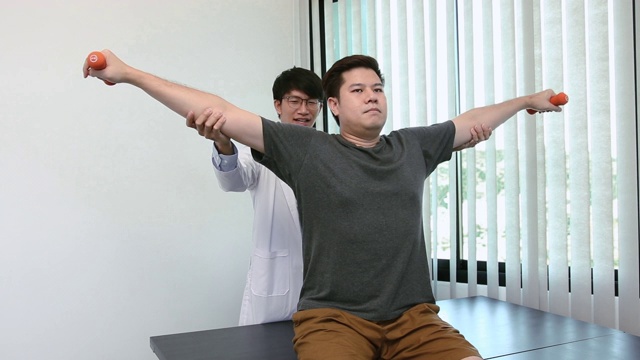 在他的康复中心，亚洲理疗师帮助病人举起手臂举起哑铃。视频素材