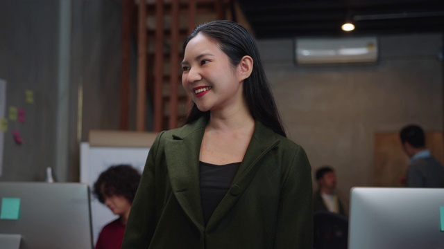 迷人的亚洲女商人微笑着看着相机，一个积极的，满意的，愉快的表情享受在一个现代的办公室成功摆姿势。视频素材