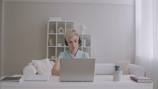 心理学家通过互联网在线咨询，女性专家坐在桌子旁对着笔记本电脑的网络摄像头说话视频素材