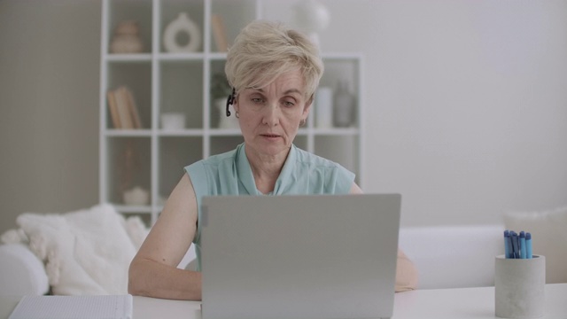 一位戴着耳机的老年妇女通过网络摄像头说话，通过视频通话在笔记本电脑上进行交流视频素材