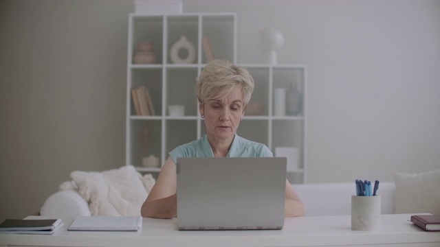 一位老年妇女坐在家里，用笔记本电脑上网聊天，和朋友聊天视频素材