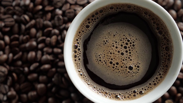 白杯的新鲜咖啡在烤咖啡豆的背景。视频下载