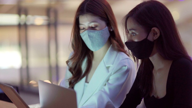 一些亚洲商业女性戴着口罩在办公室工作到深夜，并使用笔记本电脑视频素材