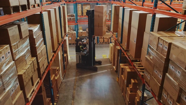 高空无人机拍摄:电动叉车卡车操作员举起托盘与纸箱在一个大零售仓库的货架。物流产品和货物配送中心视频素材