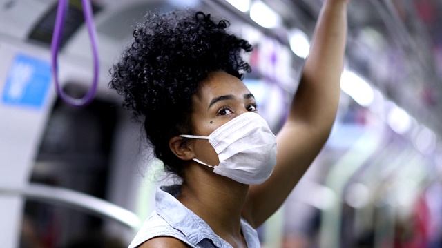 一名年轻的黑人妇女在地铁通勤时手握扶手，戴着口罩视频素材
