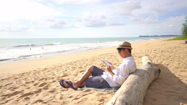年轻人在沙滩上放松的时候看书的4k视频片段视频素材