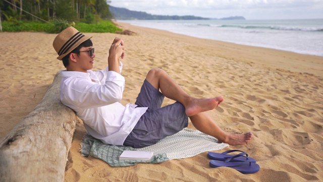 一段年轻人在海滩上休息时玩智能手机的4k视频视频素材