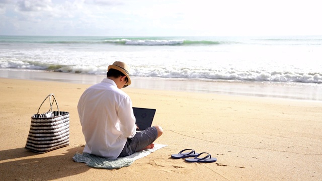一段年轻人在海滨用笔记本电脑工作，在海滩上休息时看海景的4k视频视频下载