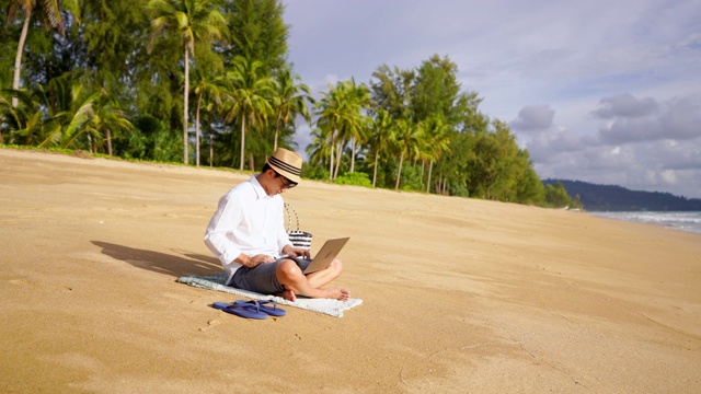 一段年轻人在海滨用笔记本电脑工作，在海滩上休息时看海景的4k视频视频素材