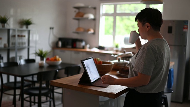 亚洲华人成熟女性在厨房用数码平板电脑上网休息视频素材