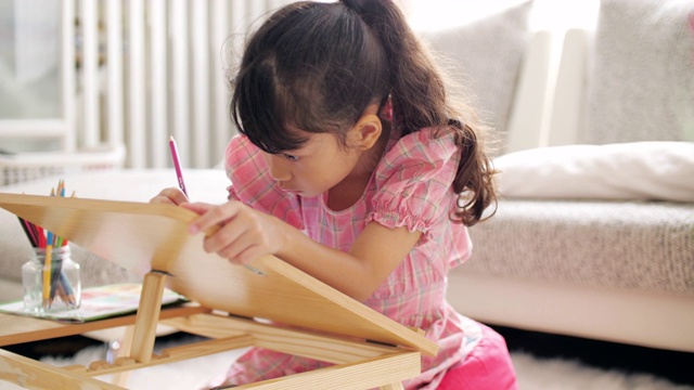 小女孩穿着粉红色的衣服，在家里的客厅里在画册上画画和写字视频素材