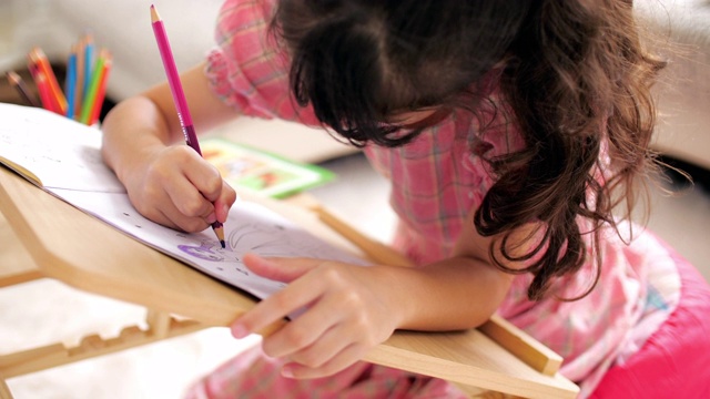 小女孩穿着粉红色的衣服，在家里的客厅里在画册上画画和写字视频素材