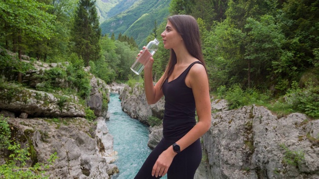 一名女子在山间河边休息，用可重复使用的水瓶补水视频下载