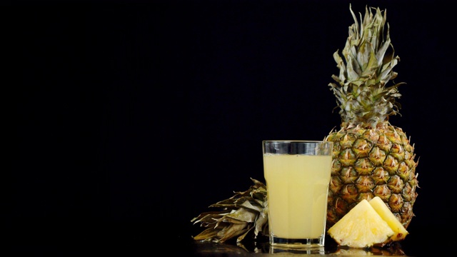 新鲜的菠萝和一杯菠萝汁慢慢旋转。视频下载
