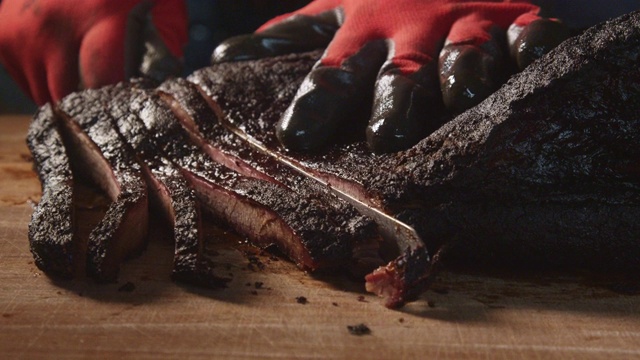 戴手套的手慢慢地切割完美烹饪的德州烧烤风格的牛胸肉在一个乡村砧板上视频下载