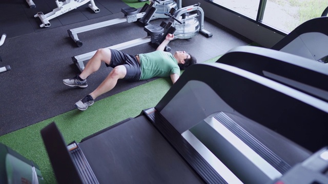 超重的书呆子在跑步机上跑累了，倒在健身房的地板上视频素材