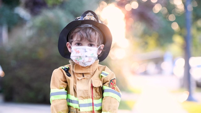 严肃的小男孩穿着万圣节消防员的服装，戴着防护面具看着镜头，手里拿着杰克灯的水桶视频素材