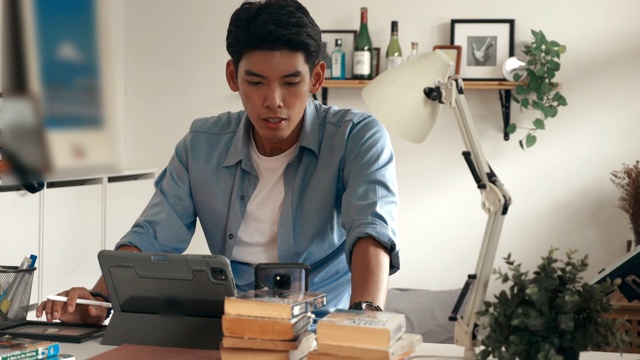 一个年轻人坐在家里的桌子旁使用平板电脑视频素材