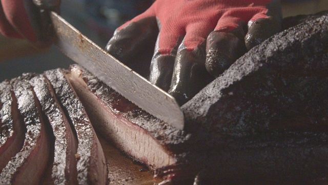 戴手套的手慢慢地切割完美烹饪的德州烧烤风格的牛胸肉在一个乡村砧板上视频素材