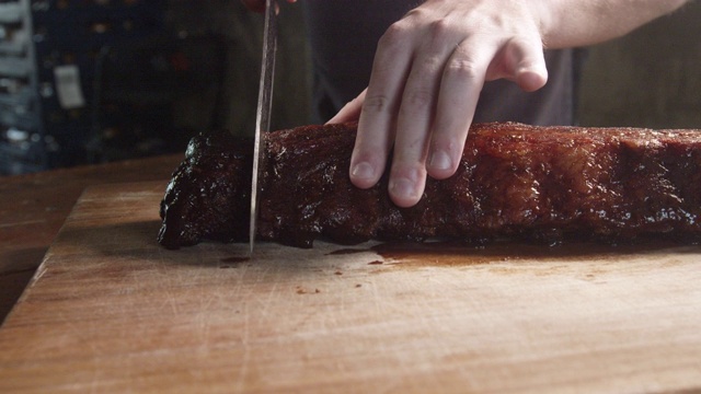 一名男子正在一个乡村木砧板上切一排新鲜烤架上的多汁猪肋排视频素材