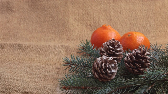 新年的成分是橘子、松果和树枝上的一棵新年树。红丝带慢慢地落在镜框里的桌子上。视频素材