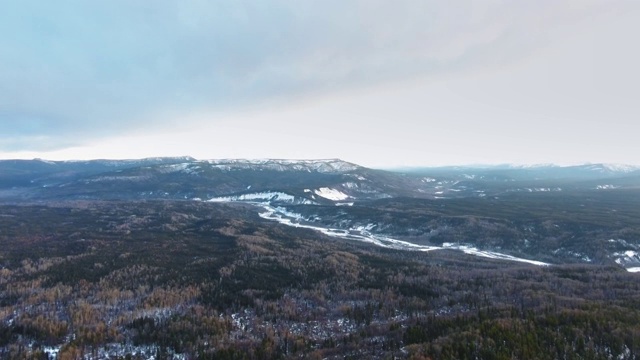 航拍在茂密的森林中冰冻的特察河，在地平线上的山脉(阿尔伯塔，加拿大)视频素材